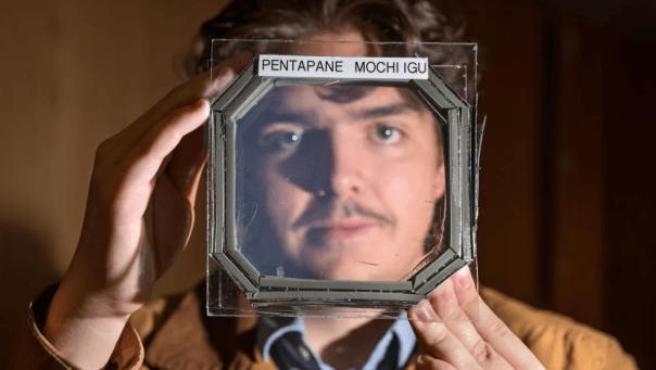 Abram Fluegel segura uma amostra quadrada composta por cinco camadas do novo material quase transparente e isolante chamado MOCHI, desenvolvido por pesquisadores do laboratório do professor de física Ivan Smalyukh na Universidade do Colorado em Boulder.