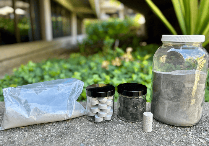 Phlego的生产工艺与现有的水泥生产方法兼容。图中展示了该工艺的各个阶段，从原材料（左侧袋子中）到符合行业标准的圆柱形Phlego砂浆样品。