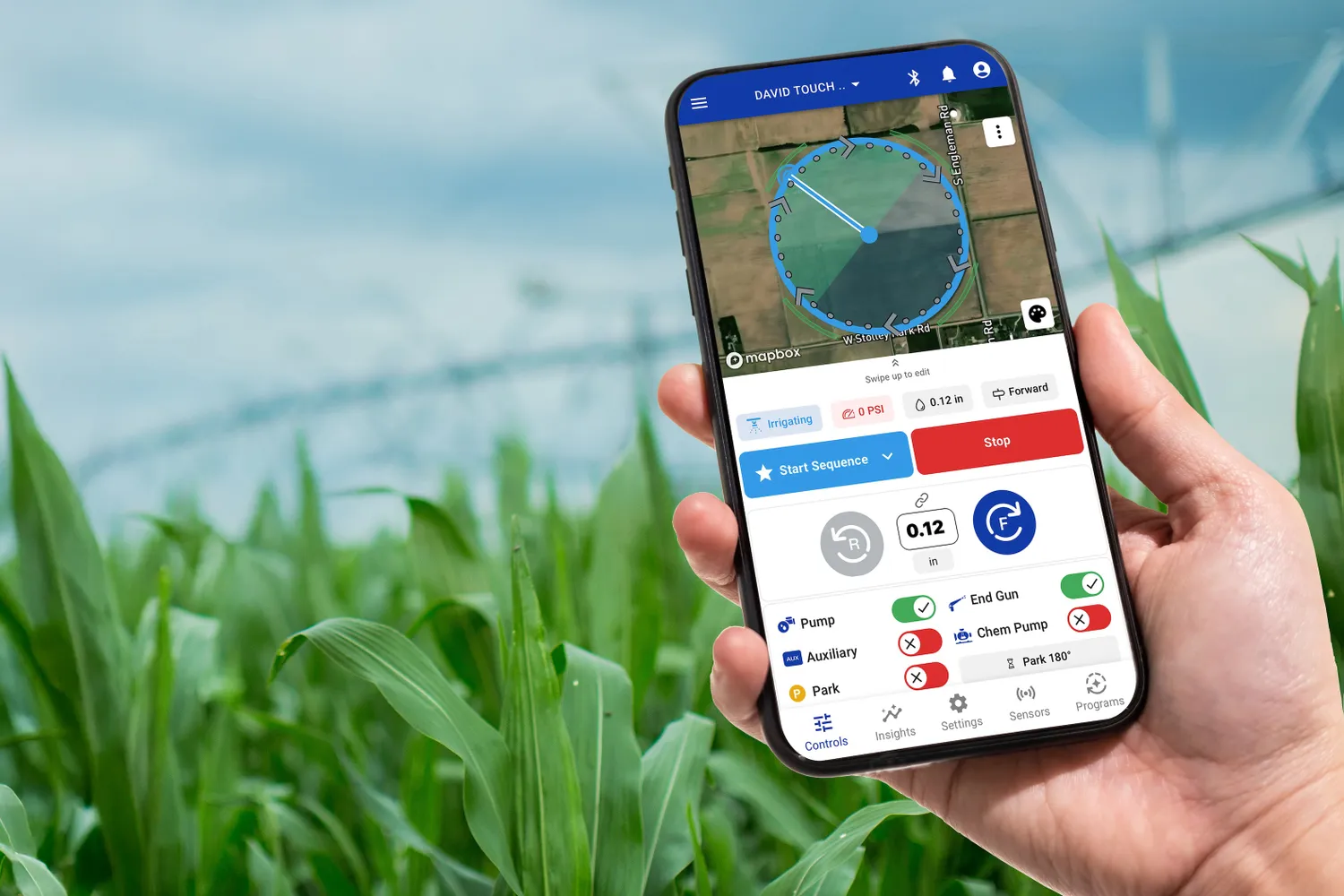 A hand holding a smartphone displaying a farming application interface over a field with crops