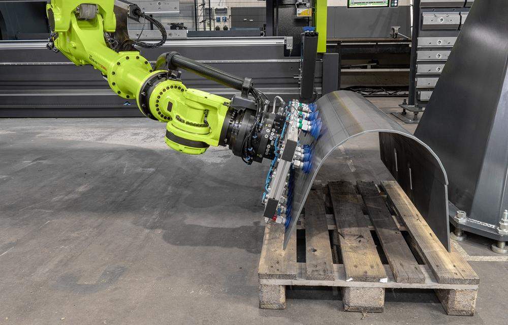 Un robot coloca una pieza metálica doblada sobre una tarima de madera.
