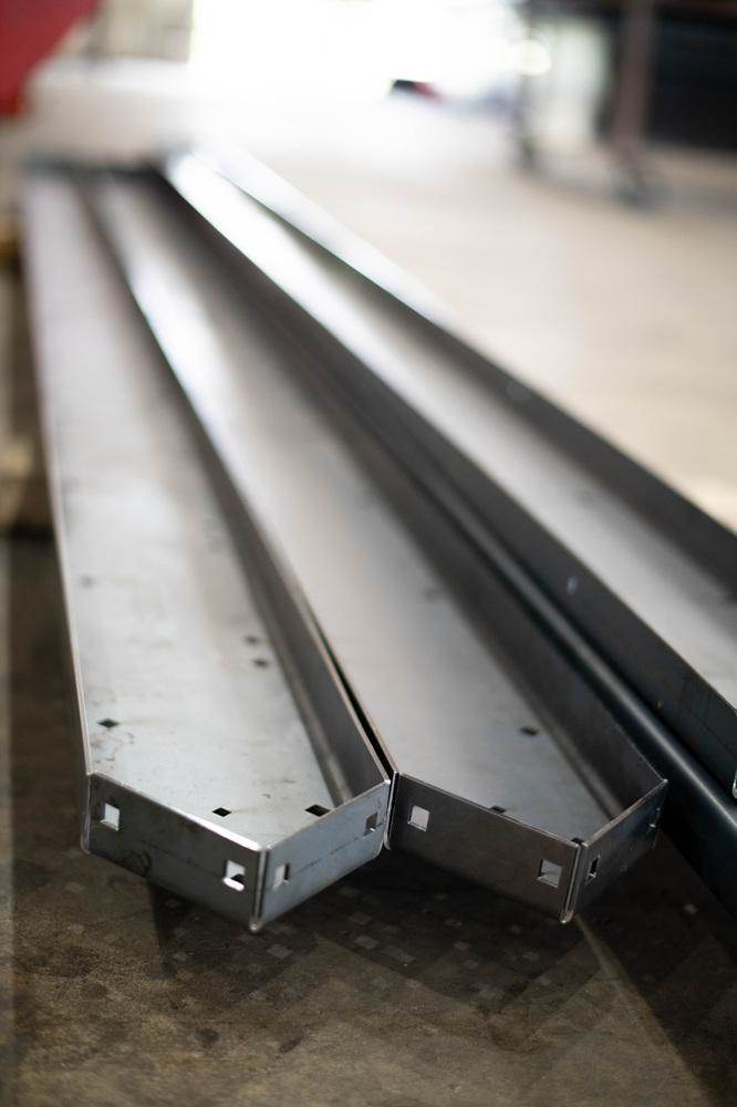 Várias peças metálicas longas sobre uma mesa, com furos cortados a laser e bordas moldadas.