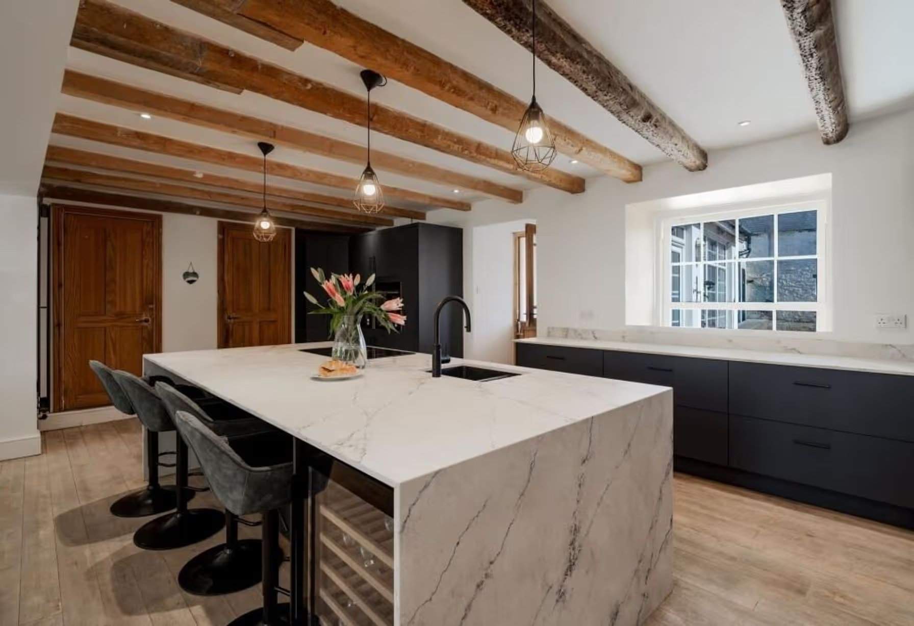 Transformation remarquable en une cuisine moderne et élégante. Le choix des couleurs et des matériaux garantit qu'elle reste chaleureuse et non froide. Les poutres apparentes au plafond et la porte apparente au fond deviennent des éléments plus caractéristiques grâce à la réduction du bois environnant. Manoir Johnston Hall près de Haverfordwest, mis en vente pour 1,85 million de livres sterling par Fine & Country West Wales (Aberystwyth)