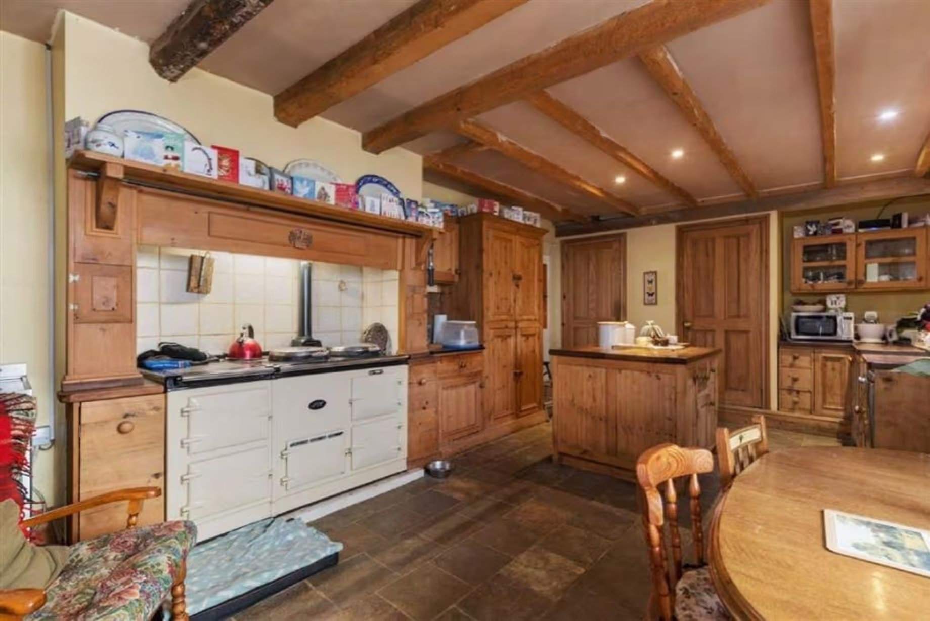 Cuisine avant rénovation, de style campagnard classique avec poutres apparentes, abondance de boiseries en pin apparent et cuisinière AGA double face. Manoir Johnston Hall près de Haverfordwest, mis en vente pour 1,85 million de livres sterling par Fine & Country West Wales (Aberystwyth)