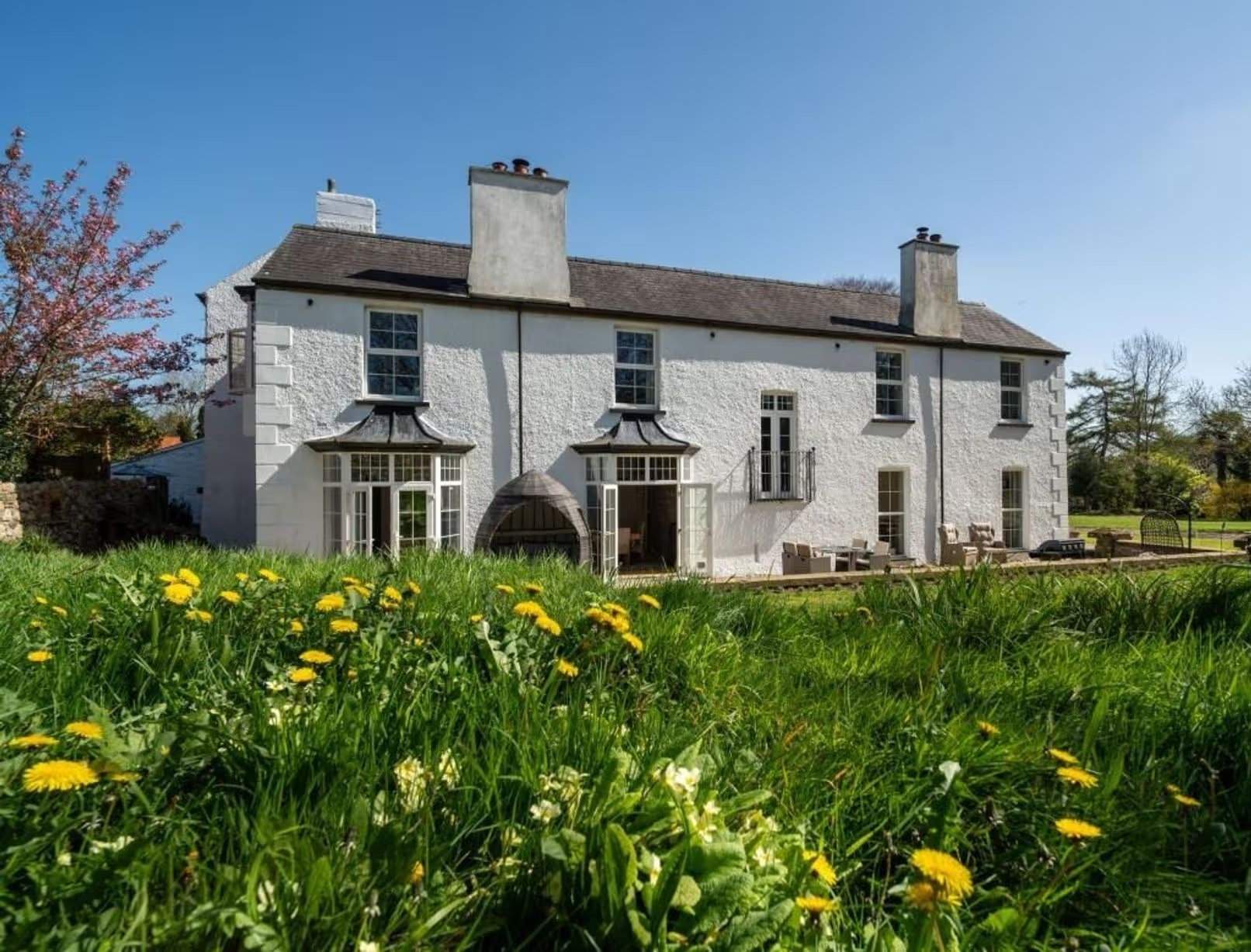 Vue extérieure du manoir Johnston Hall peint en blanc, près de Haverfordwest, mis en vente pour 1,85 million de livres sterling par Fine & Country West Wales (Aberystwyth), entouré de jardins paysagers matures