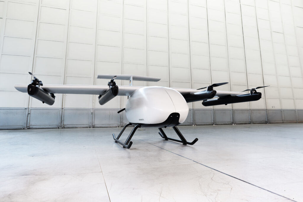 Drone quadrirotor blanc avec train d’atterrissage stationné dans un hangar propre et vide.