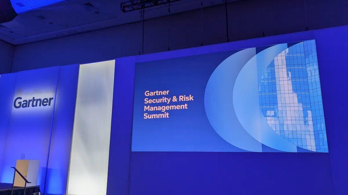 Gartner 标识显示在蓝色灯光墙上,旁边屏幕显示“Gartner 安全与风险管理峰会”字样