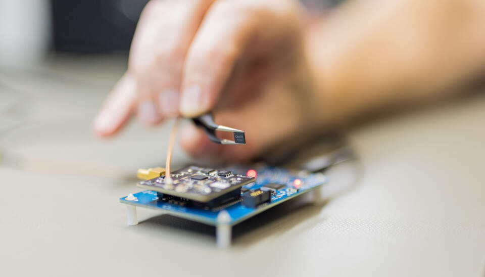Tweezers holding a Qualinx QLX3xx chip above a circuit board