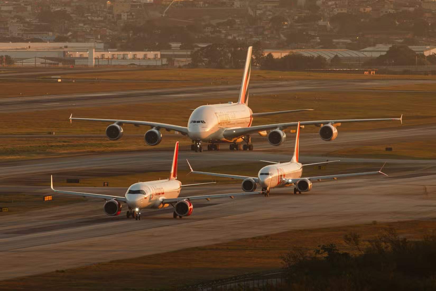 飞机队列,包括空客A320、波音737-800和阿联酋航空A380,在巴西圣保罗瓜鲁柳斯机场日落时分