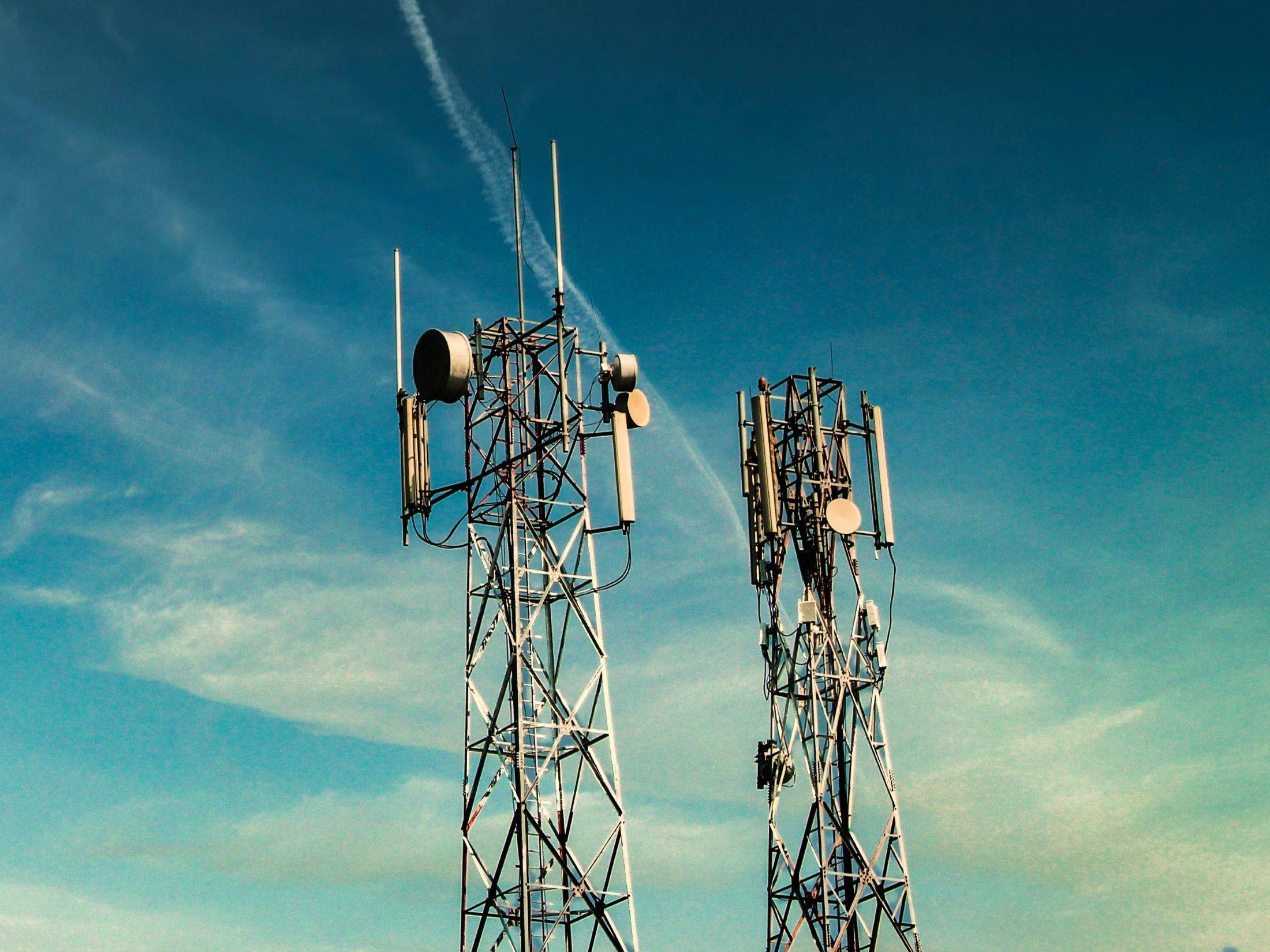 Two telecom masts equipped with macro and microwave antennas against a clear sky, representing the physical infrastructure managed by Federated Wireless Spectrum AI for CBRS network capacity.