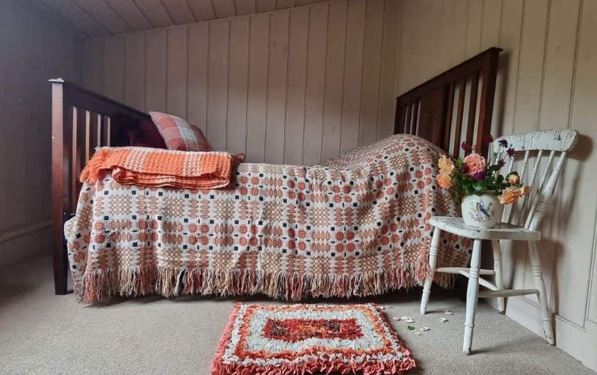 Jane Beck Welsh Blankets in ihrem renovierten Zuhause in der Nähe von Tregaron, Ceredigion. Dies ist eines von fünf Schlafzimmern mit einem traditionellen dunklen Holzbett und orangefarbenen und cremefarbenen traditionellen walisischen Decken. Die Renovierung dauerte 29 Jahre, und sie hatte anfangs nur 23 Pfund in der Tasche.