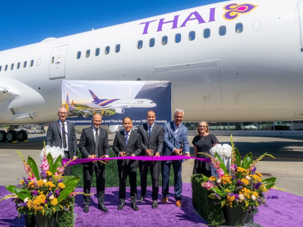 Un groupe de dirigeants coupe un ruban violet devant un avion de Thai Airways, avec des compositions florales colorées à côté de la cérémonie