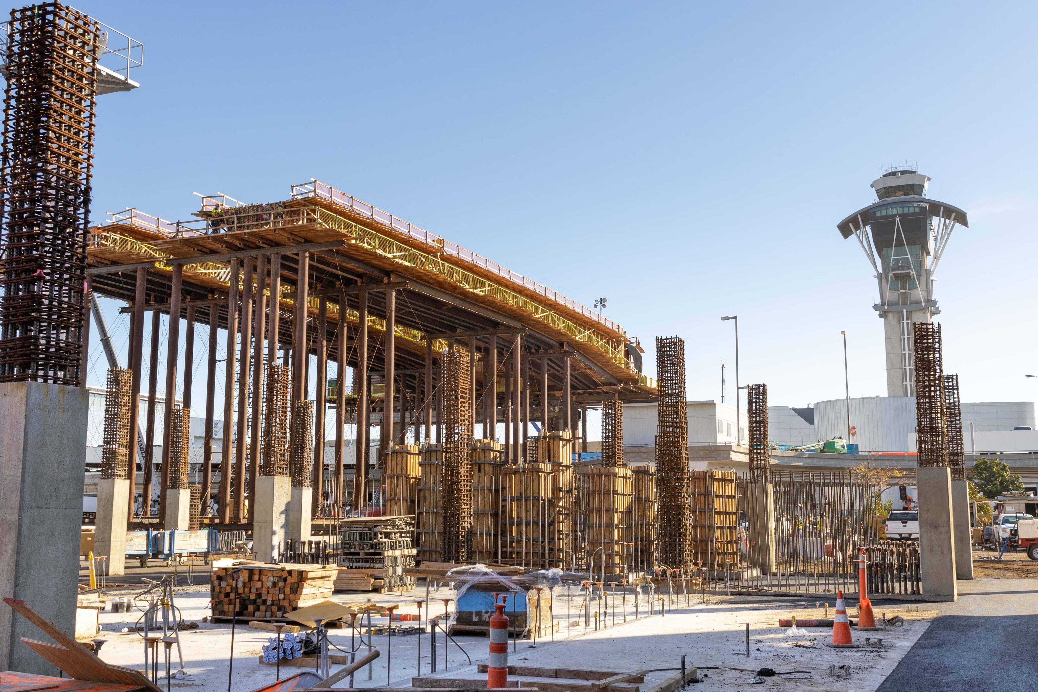 En la futura estación del área de terminales del oeste-centro, los trabajadores de construcción continúan avanzando con la instalación de los rieles guía, mientras construyen pilares de soporte para el nuevo estacionamiento.