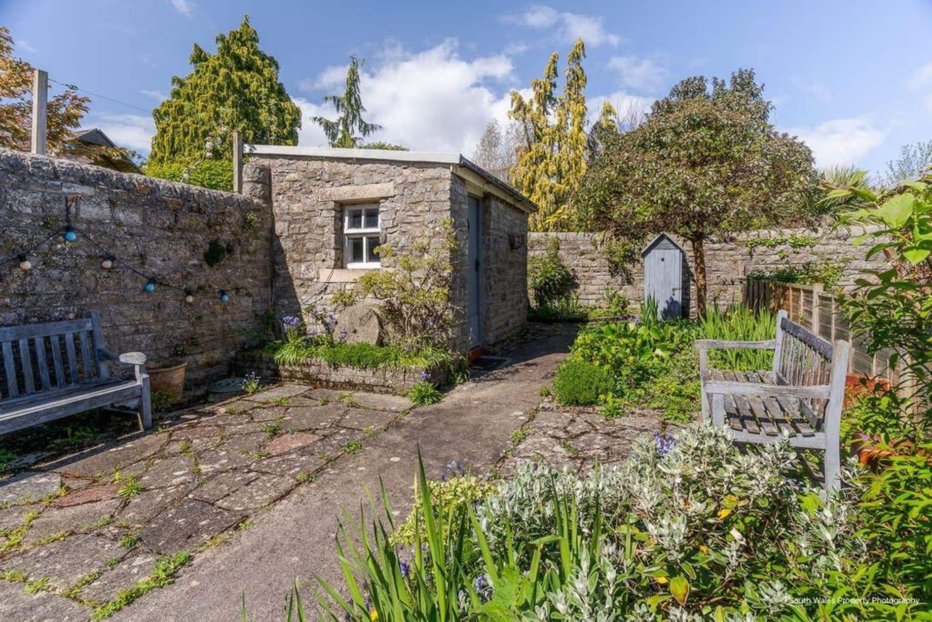 Charming walled garden offering peace and privacy, yet located in the heart of the bustling seaside town of Penarth, featuring a wooden bench and flagstone flooring, Victorian end-terrace coastguard cottage, Grade II listed, for sale by David Baker (Penarth) with a guide price of over £400,000