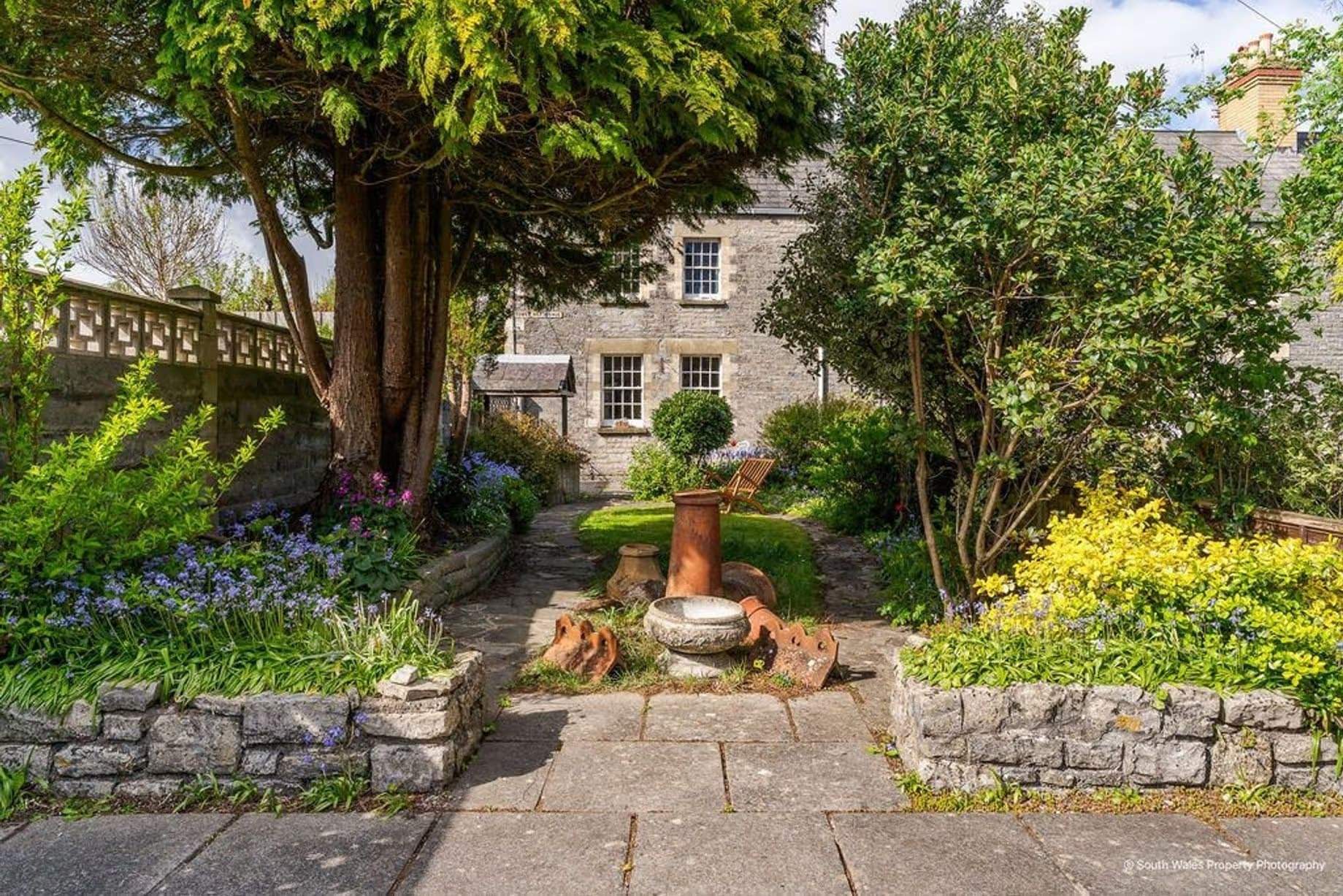 Charming entrance to the house from the parking area, with ancient flagstones and mature plants hinting at the cottage