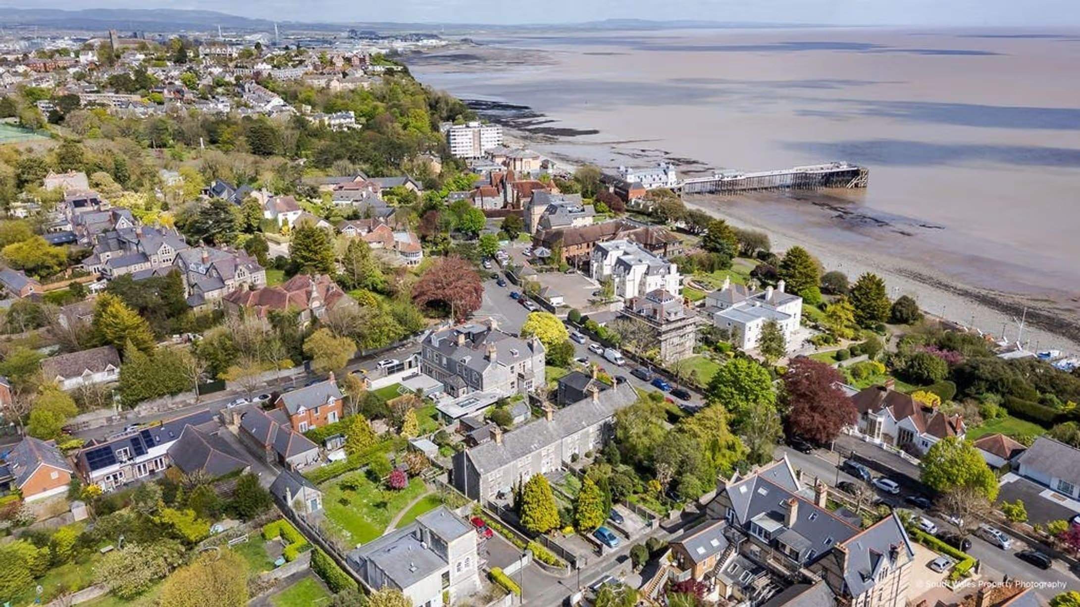 Aerial photograph showing the row of cottages is within walking distance of the promenade, beach, and pier, one of many buildings in the original coastguard complex, which also included a lookout tower (now a fine residence), a rocket cart house, and a powder magazine for storing distress flares, Victorian end-terrace coastguard cottage, Grade II listed, for sale by David Baker (Penarth) with a guide price of over £400,000