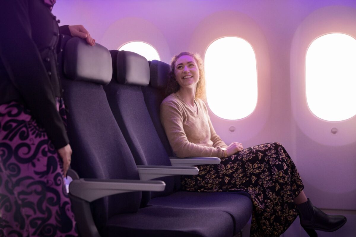 Woman sitting in a purple-lit cabin, smiling at a flight attendant standing beside her seat