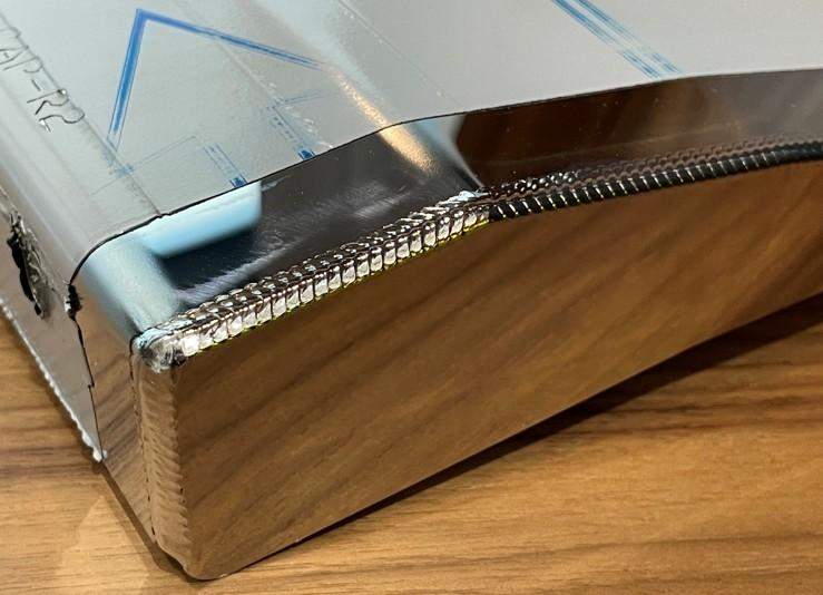 Uma solda a laser em uma peça de aço inoxidável polida é destacada.
